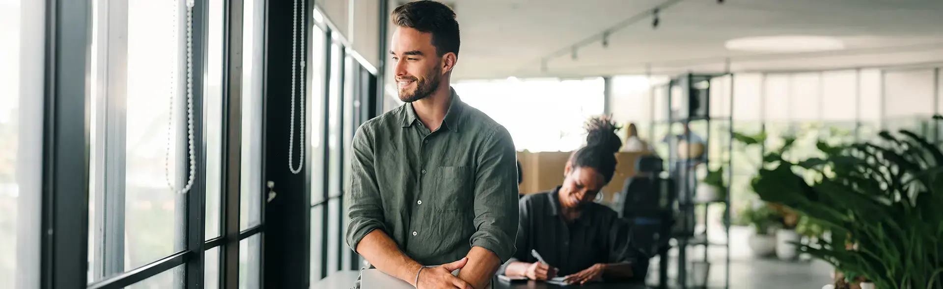 "Software engineer holding a laptop in a modern Brisbane office, with a colleague working at a desk in the background
